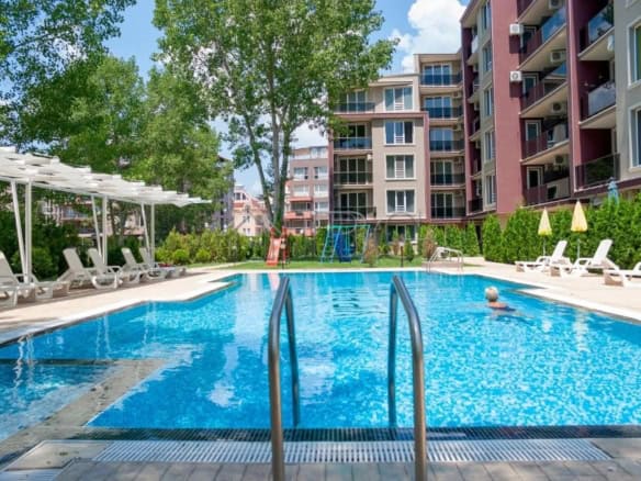 Modern apartment pool with garden and residential buildings in the background.