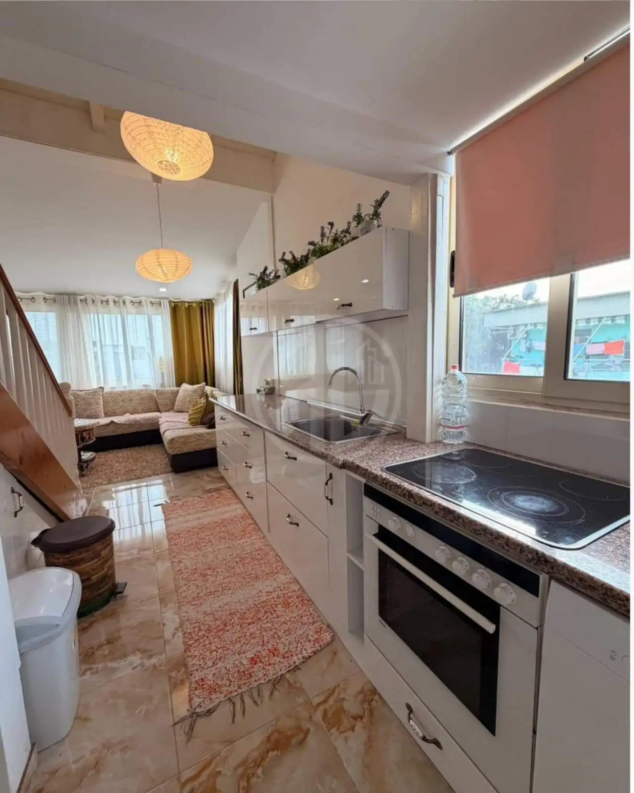Modern kitchen with white cabinets and granite countertops, adjacent to a bright living room with la.