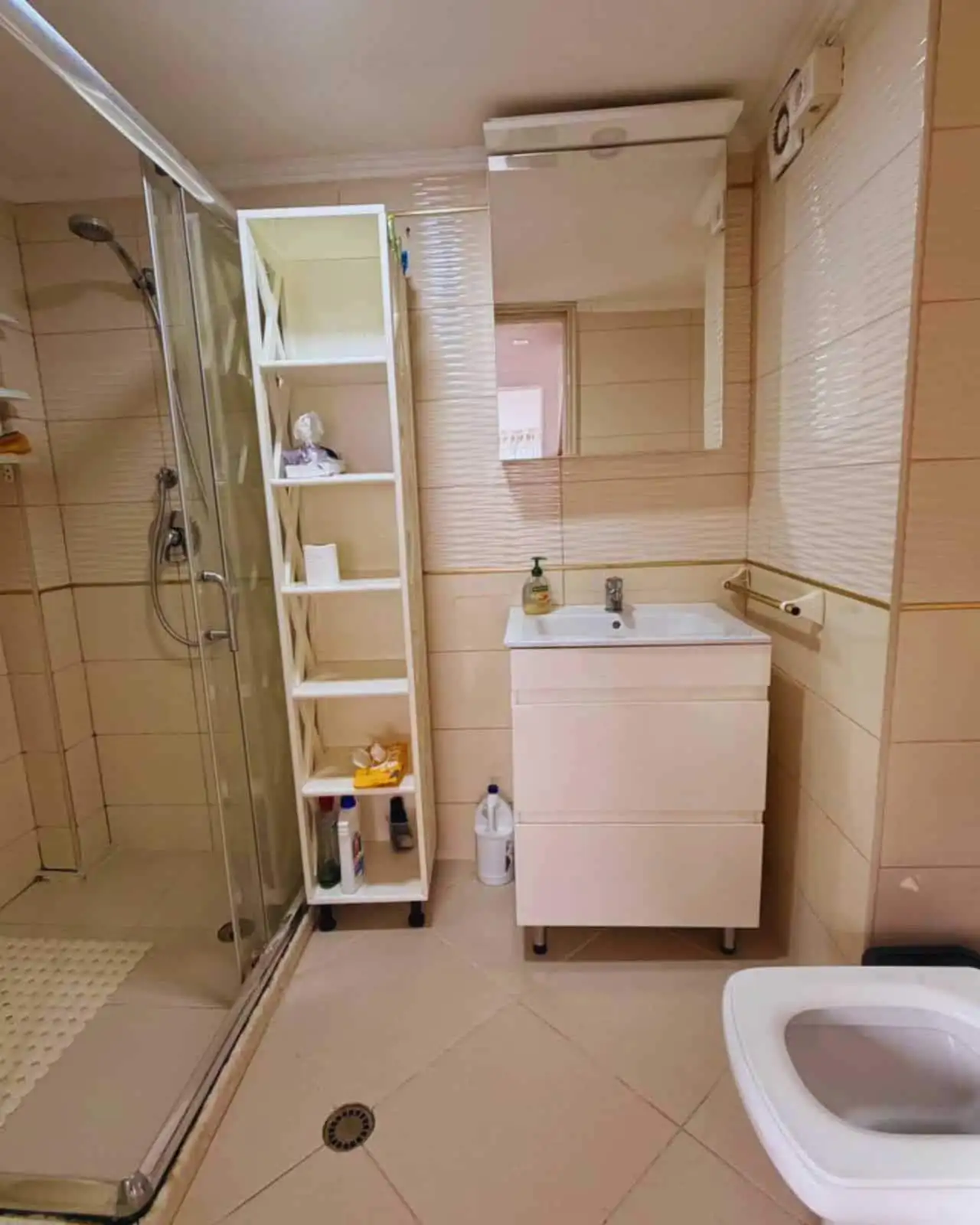 Bathroom with shower, sink, mirror, and storage shelves.