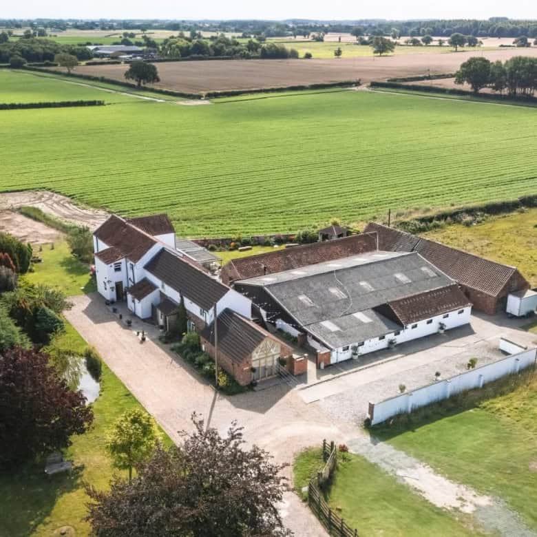 Aerial view of a rural farmhouse surrounded by lush green fields and farmland, showcasing ample outd.