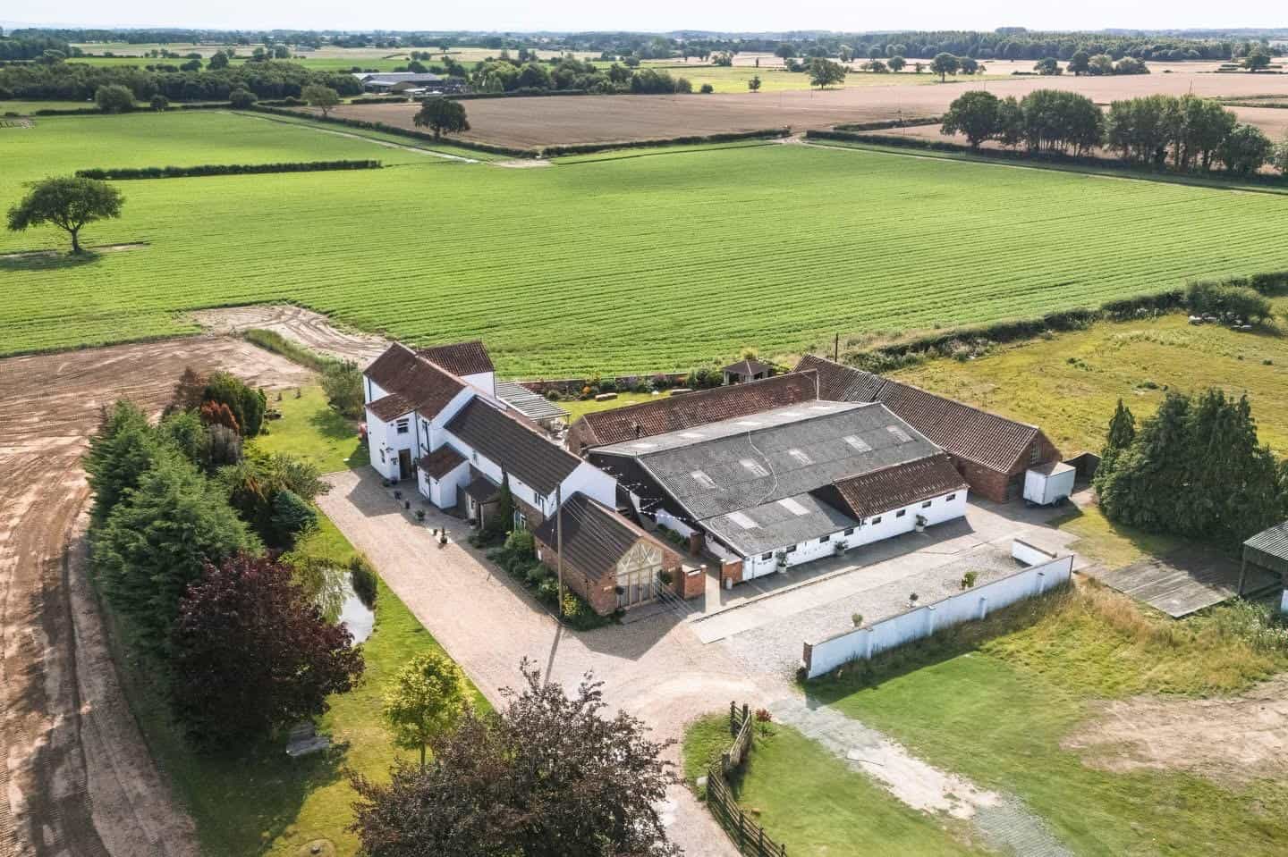 Country Farmhouse with Spacious Land and Outbuildings Aerial view of a rural farmhouse surrounded by lush green fields and farmland, showcasing ample outd.