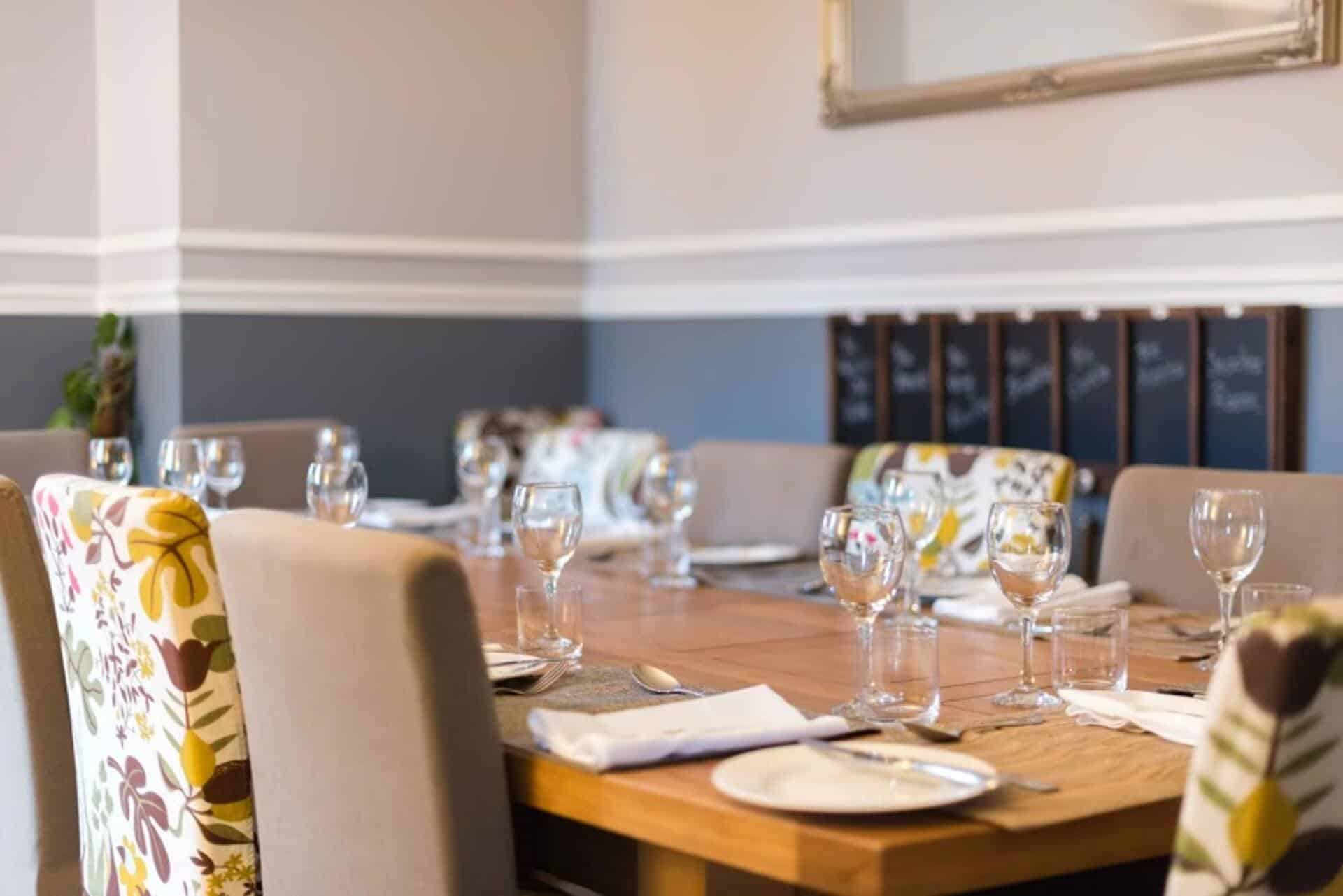 Modern dining room with elegant table setting and floral upholstered chairs. Elegant dining room with a wooden table, glassware, and floral-patterned chairs for a sophisticated.