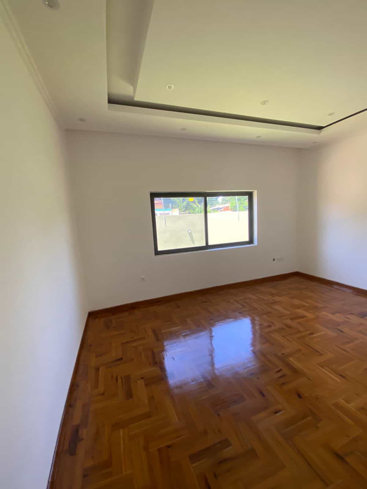 Spacious empty room with wooden floors and a large window for natural light.