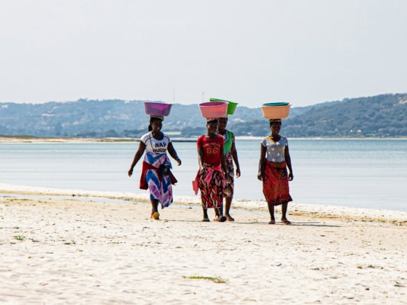 Women walking on Mozambique beach carrying baskets on their heads.