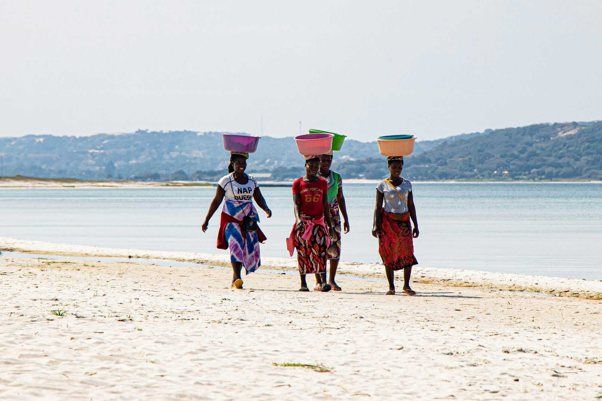Women walking on Mozambique beach carrying baskets on their heads.