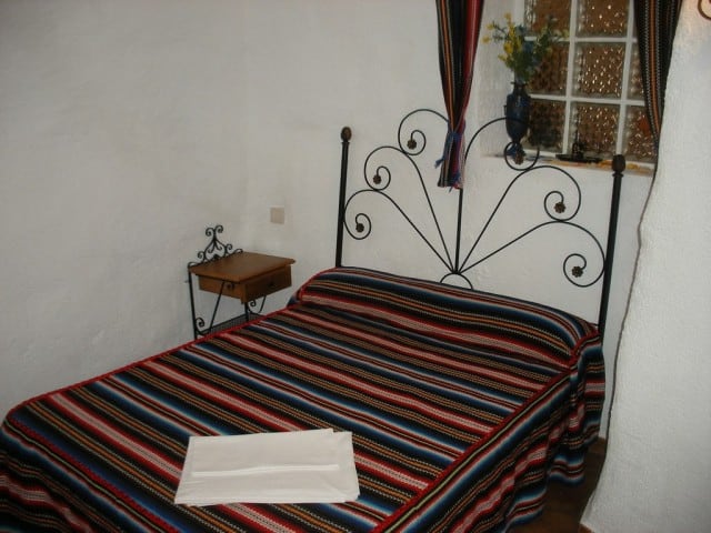 Cozy cave house bedroom with wrought iron bed and colorful striped bedding in Granada.