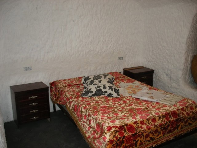 Cozy bedroom inside a cave house in Cuevas del Campo, Granada, with floral bedding and rustic walls.