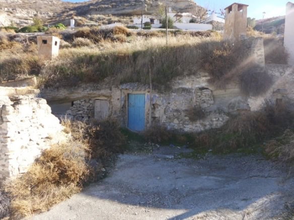 Cave house with blue door in Galera, Granada, surrounded by dry landscape and hillside.