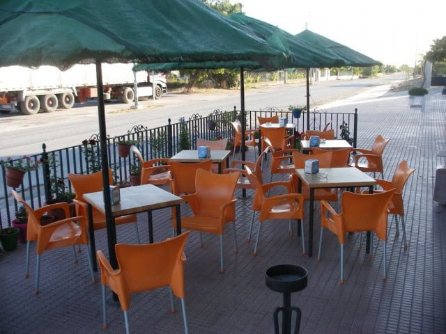 Outdoor café tables and orange chairs under green umbrellas in a commercial area.