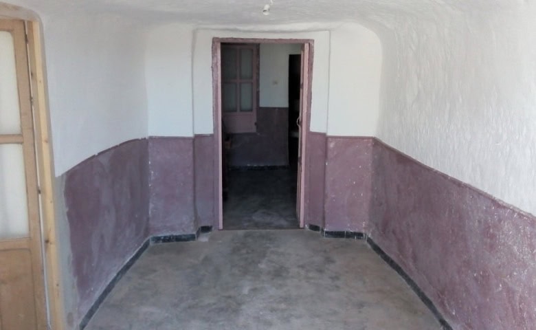 Interior view of a traditional cave house in Freila, Granada, showcasing rustic walls and doorway.
