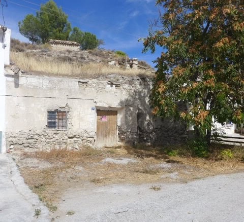 Cave house in La Alqueria, Granada with rustic stone walls and surrounding natural landscape.