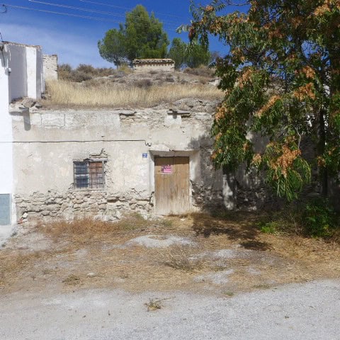 Cave house in La Alqueria, Granada with rustic exterior and surrounding greenery.