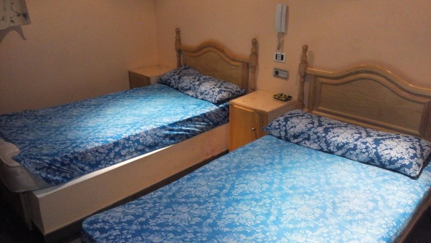 Twin beds in a hotel room in Baza, Granada, with wooden headboards and blue patterned bedding.