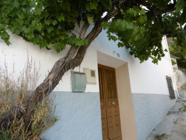 Charming village house with white walls and wooden door in Belerda, Jaen, surrounded by lush greener.