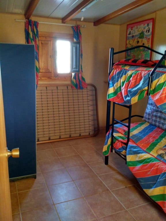 Interior of a log home bedroom with bunk beds and colorful curtains in Freila, Granada.