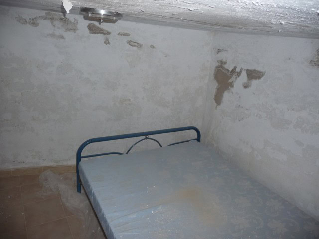 Interior of a rustic bedroom in Baza, Granada with peeling walls and a simple metal bed frame.
