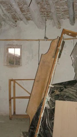 Rural property interior with unfinished walls and ceiling, construction materials, and a window show.