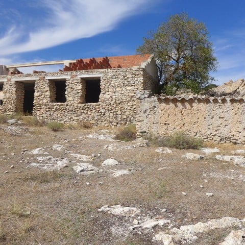 Ancient stone ruin in Cullar, Granada, with a large tree nearby under a blue sky.