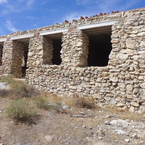 Old stone ruin in Cullar, Granada with open windows and clear blue sky.