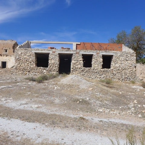 Ruin in Cullar, Granada with stone walls and open doorways under a blue sky.