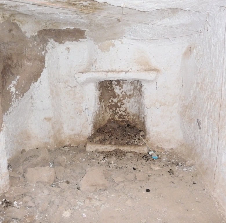 Cave house interior in Freila, Granada, showing rustic stone walls and a small fireplace.