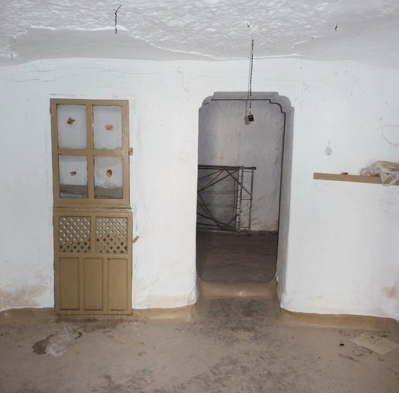 Cave house interior with whitewashed walls and rustic wooden door in Freila, Granada. Unique living.