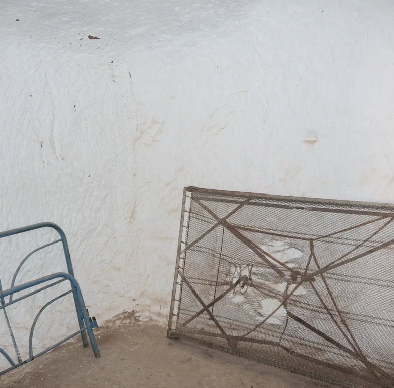 Cave house exterior in Freila, Granada with metal bed frame and rustic white wall.