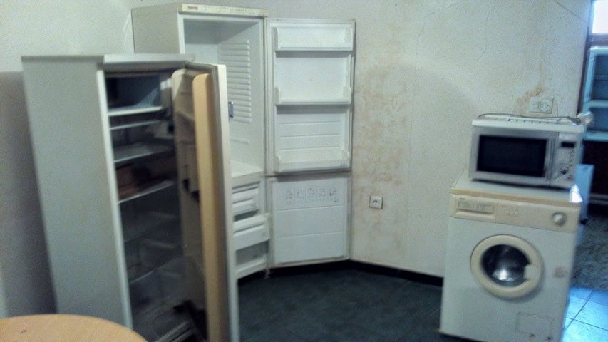 Interior view of a small kitchen with an open refrigerator, microwave, and washing machine.