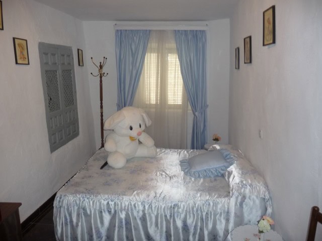 Charming bedroom with plush teddy bear, blue curtains, and vintage decor in Zujar, Granada.