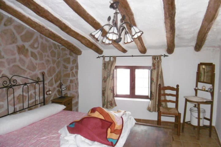 Charming bedroom with rustic stone walls, wooden beams, and vintage furniture in a village property.