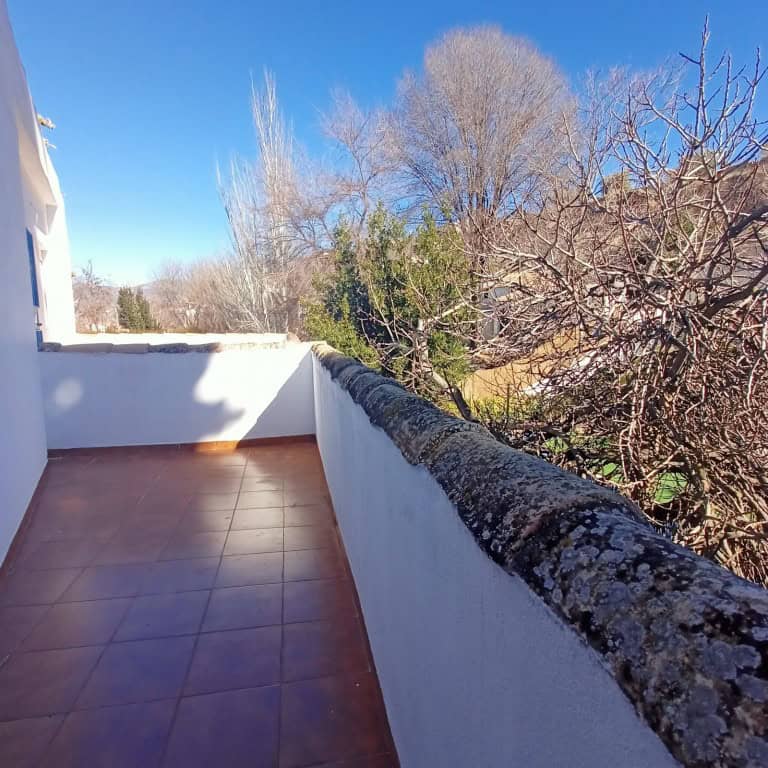 Balcony view of a town house in Fontanar, surrounded by trees and clear blue sky.