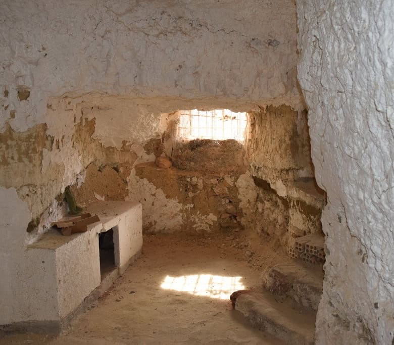 Interior view of a traditional cave house in Cuevas del Campo, Granada, showcasing rustic stone wall.