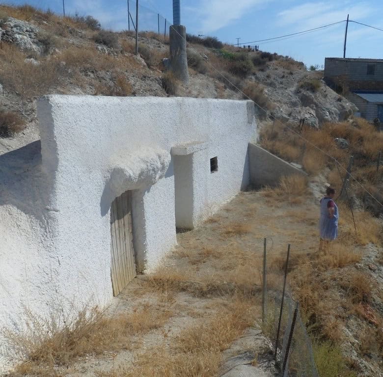 Cave house exterior in Cuevas del Campo, Granada, with whitewashed walls and rustic wooden door.