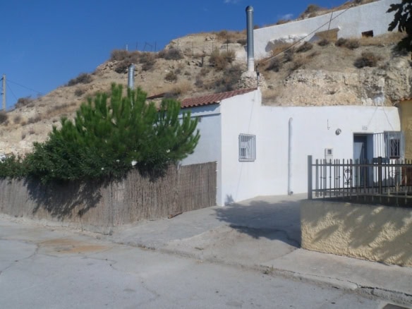 Traditional cave house in Cuevas del Campo, Granada, with white exterior walls and hillside surround.