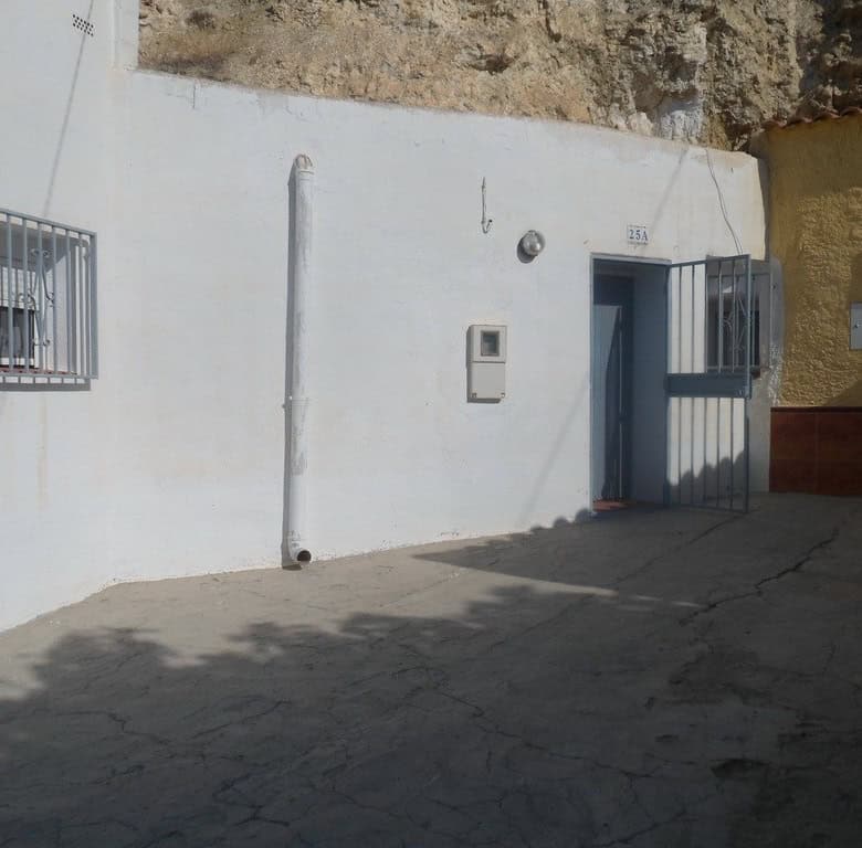 Cave house facade with white walls and barred windows in Cuevas del Campo, Granada.