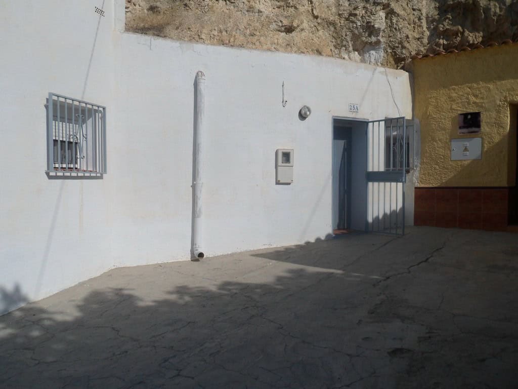 Cave house facade with white walls and barred windows in Cuevas del Campo, Granada.