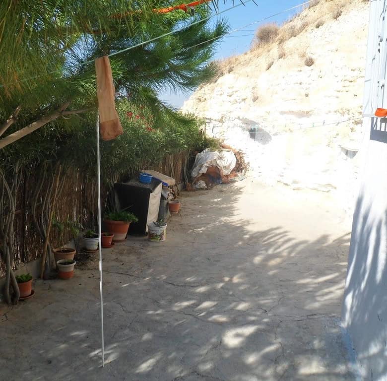 Cave house exterior in Cuevas del Campo, Granada, with potted plants and shaded pathway.
