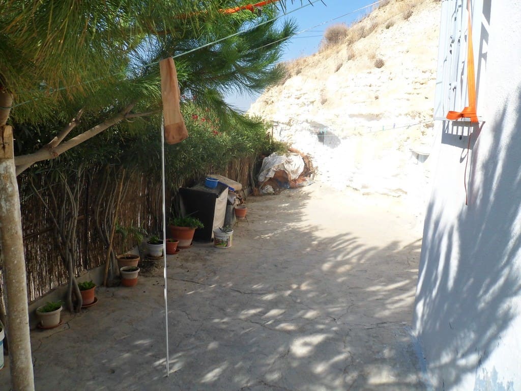 Cave house exterior in Cuevas del Campo, Granada, with potted plants and shaded pathway.
