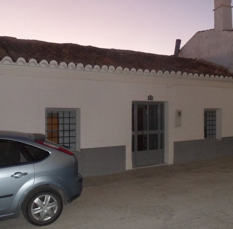 Cave house located in Freila, Granada, with traditional white exterior and surrounding vehicles.