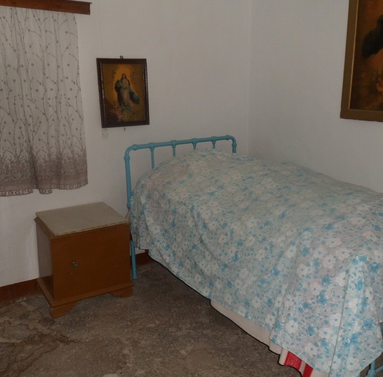 Cave house interior in Freila, Granada, featuring a cozy bedroom with a blue metal bed frame and tra.