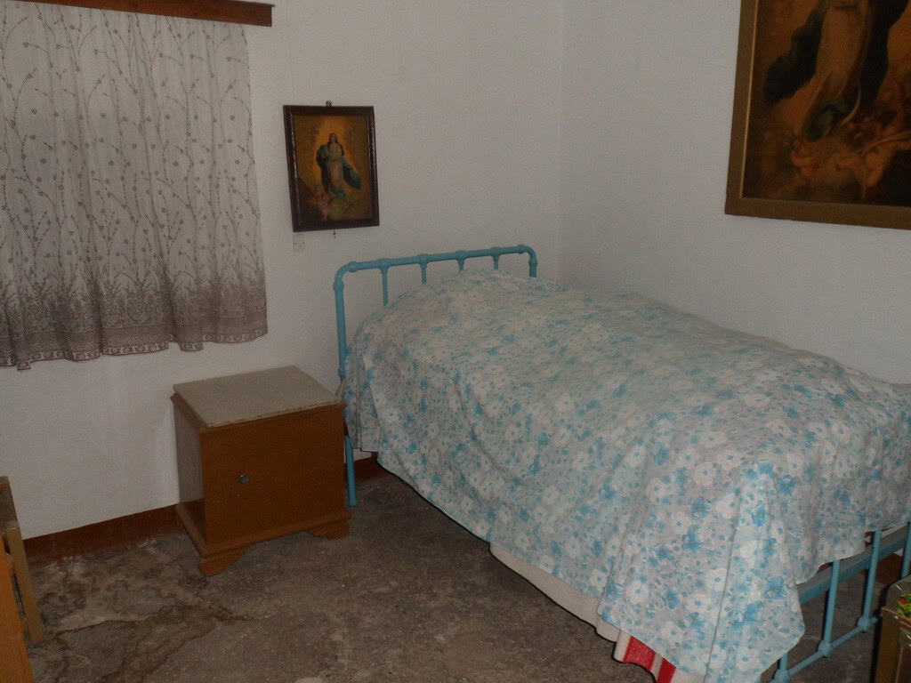 Cave house interior in Freila, Granada, featuring a cozy bedroom with a blue metal bed frame and tra.