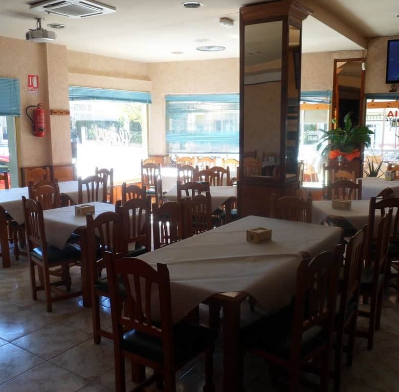 Interior of a cozy restaurant with wooden furniture and large windows in Cuevas del Campo, Granada.