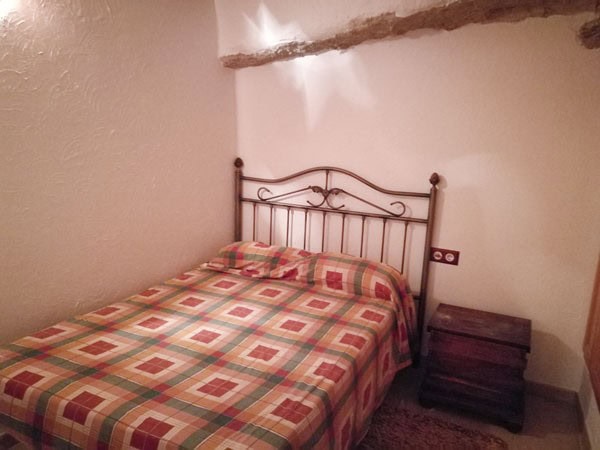 Cave house bedroom with a metal bed frame and colorful checkered bedding in Galera, Granada.