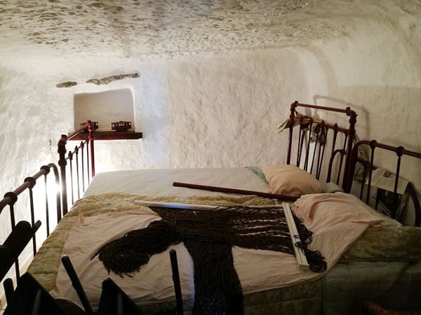 Cave house bedroom with rustic iron beds in Galera, Granada, featuring natural cave walls and cozy d.