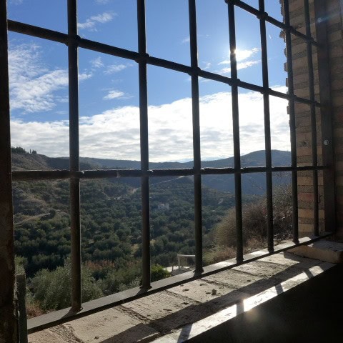 Panoramic view from a town house window in Castril, Granada, showcasing lush green hills and blue sk.