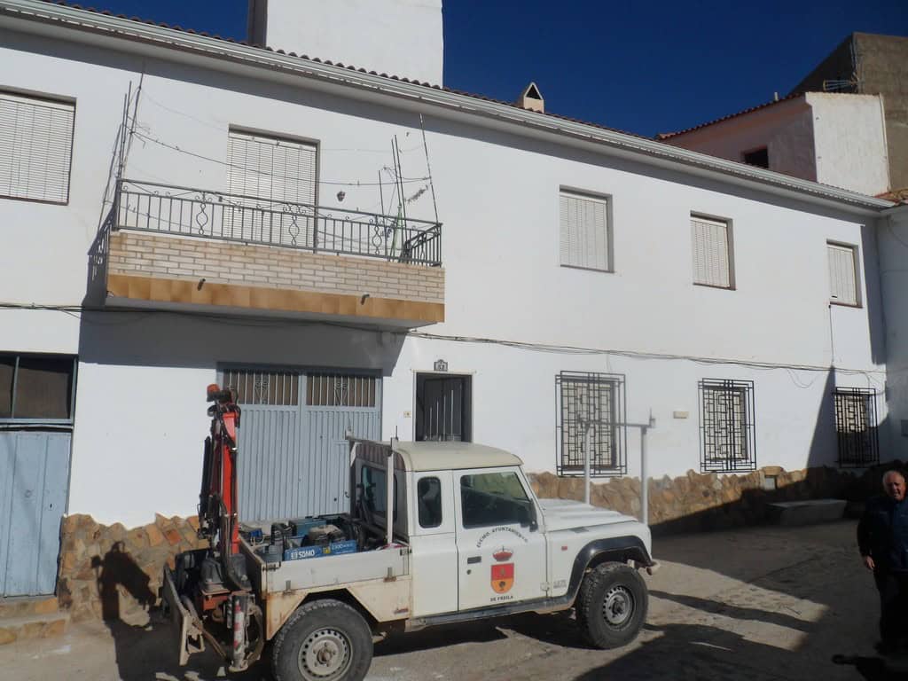 Cave house in Freila, Granada, with a white exterior and a small balcony, set against a clear blue s.