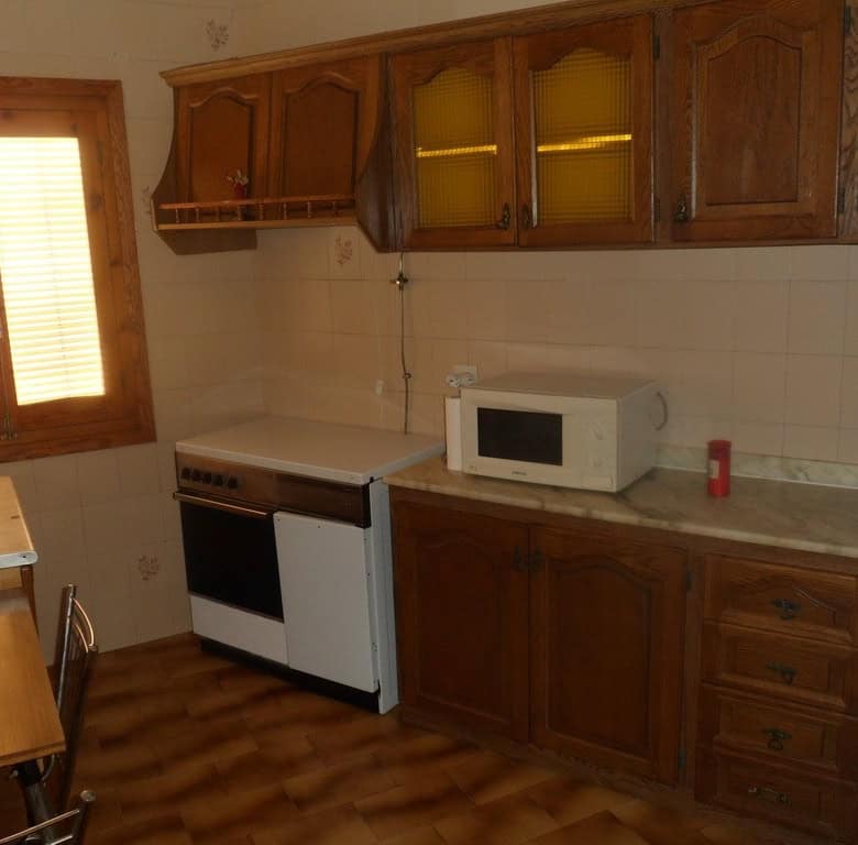Cave house kitchen with wooden cabinets, stove, microwave, and window in Freila, Granada.