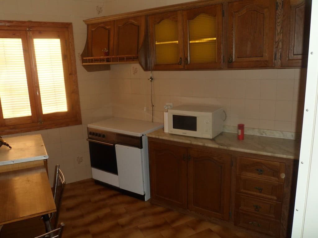 Cave house kitchen with wooden cabinets, stove, microwave, and window in Freila, Granada.