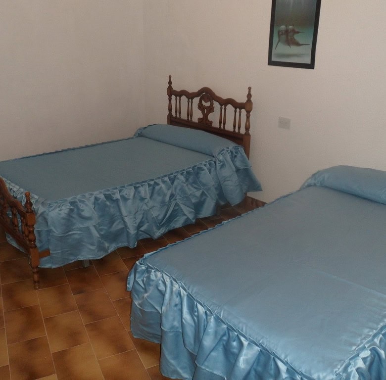 Charming bedroom in a cave house in Freila, Granada, featuring two single beds with blue bedspreads.