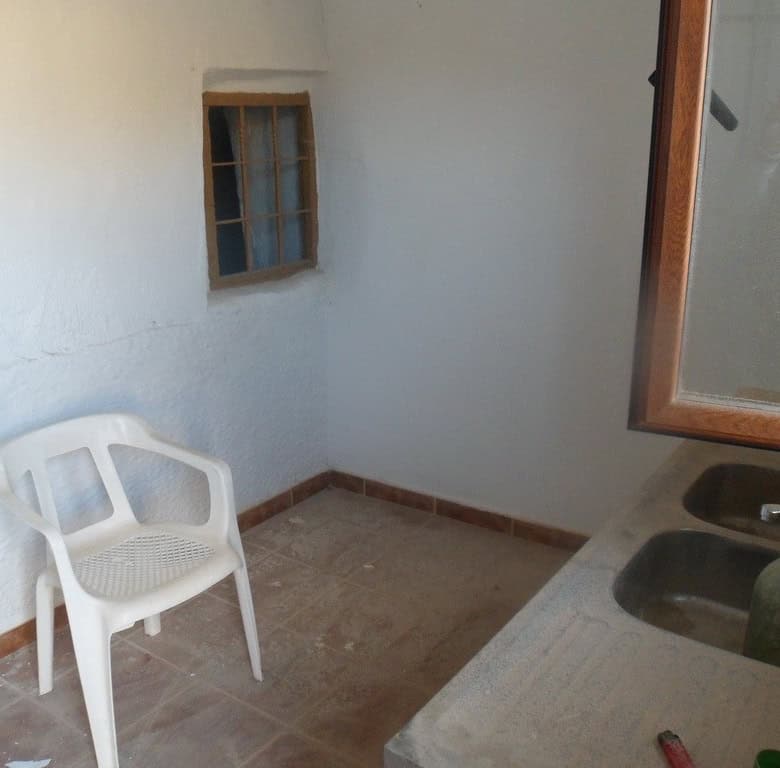 Charming cave house interior in Freila, Granada, featuring rustic walls, small window, and simple fu.